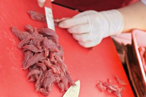 action of cutting slices of raw meat on red board